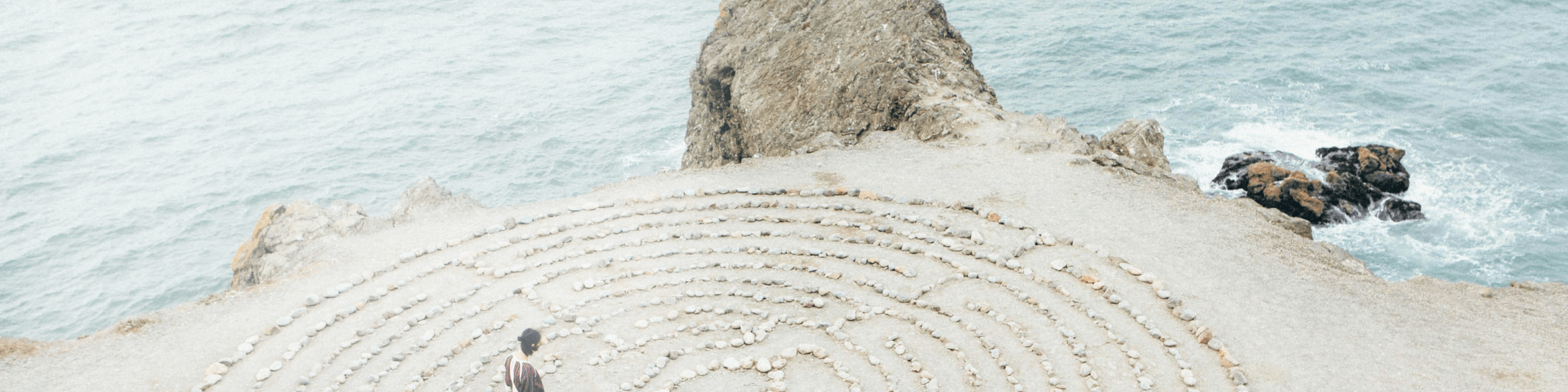 Frau läuft am Strand durch Steinlabyrinth